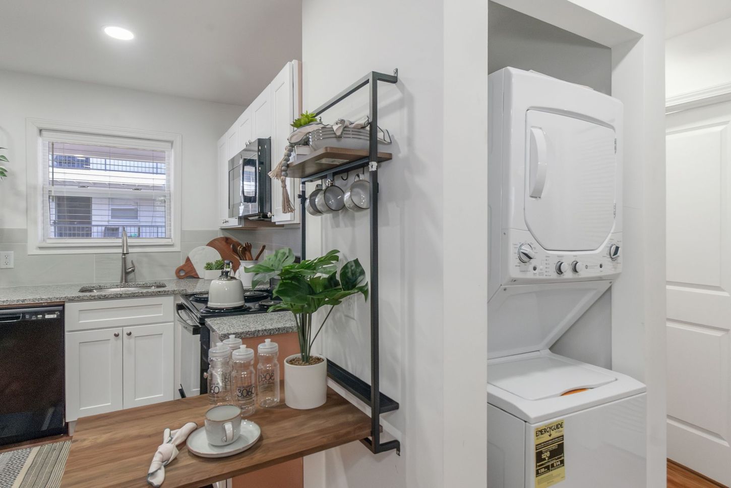 Small kitchen with white cabinets, a black stove, and a stacked washer-dryer beside a pantry.