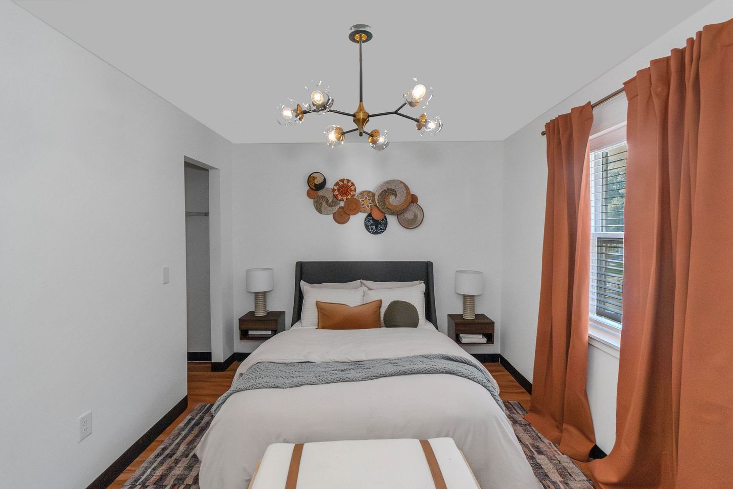 Bright bedroom with a gray bed, orange curtains, chandelier, and abstract wall art
