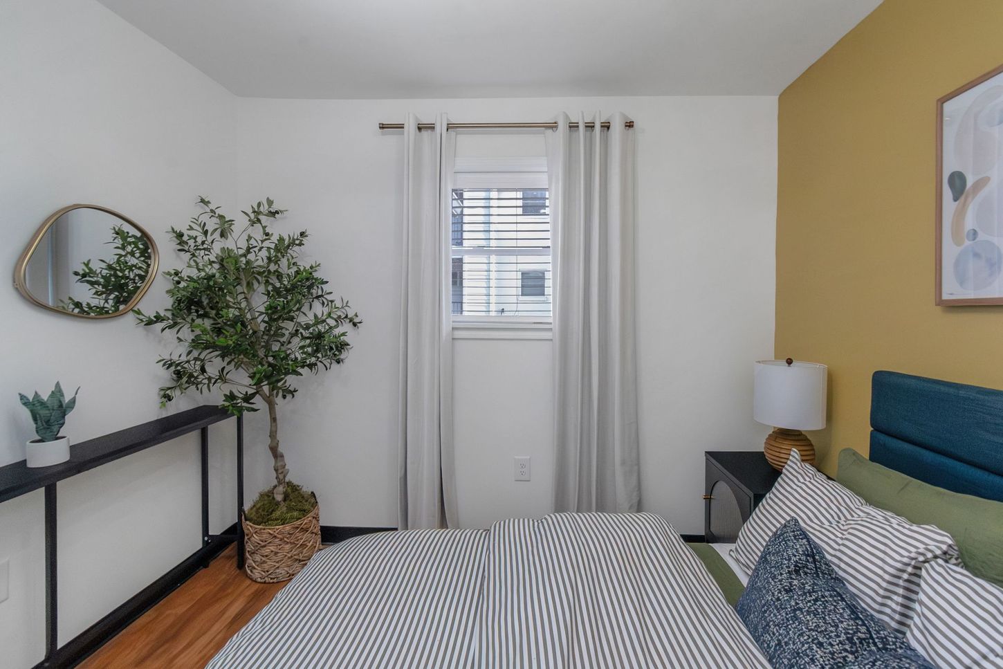 Bright bedroom with striped bed, blue headboard, window, plant, and black console table