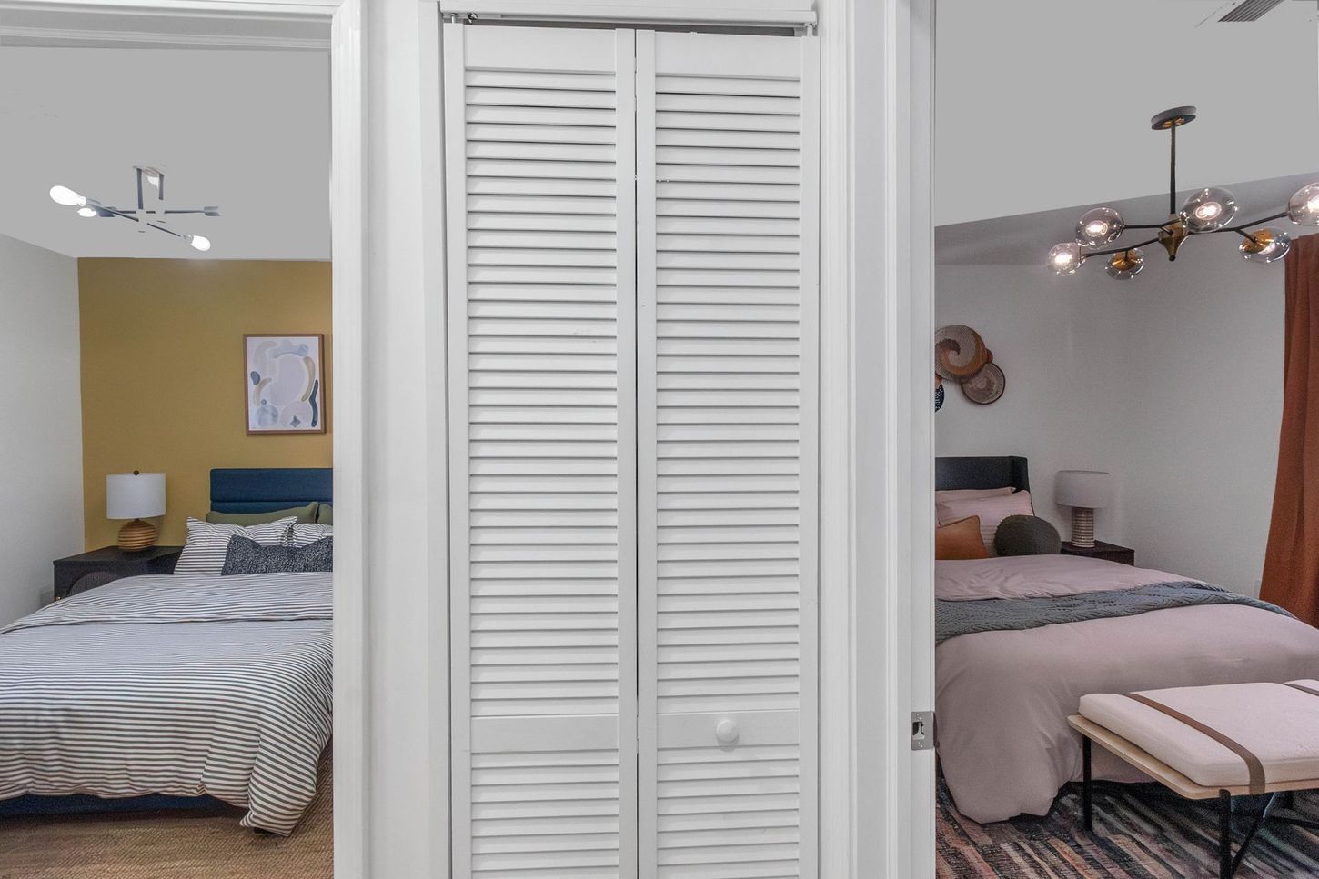 Two cozy bedrooms visible through a white louvered closet door, with beds, lamps, and ceiling fans.