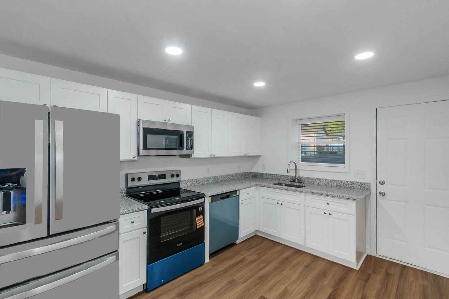 Modern white kitchen with stainless steel appliances, granite counters, blue dishwasher, and wood flooring