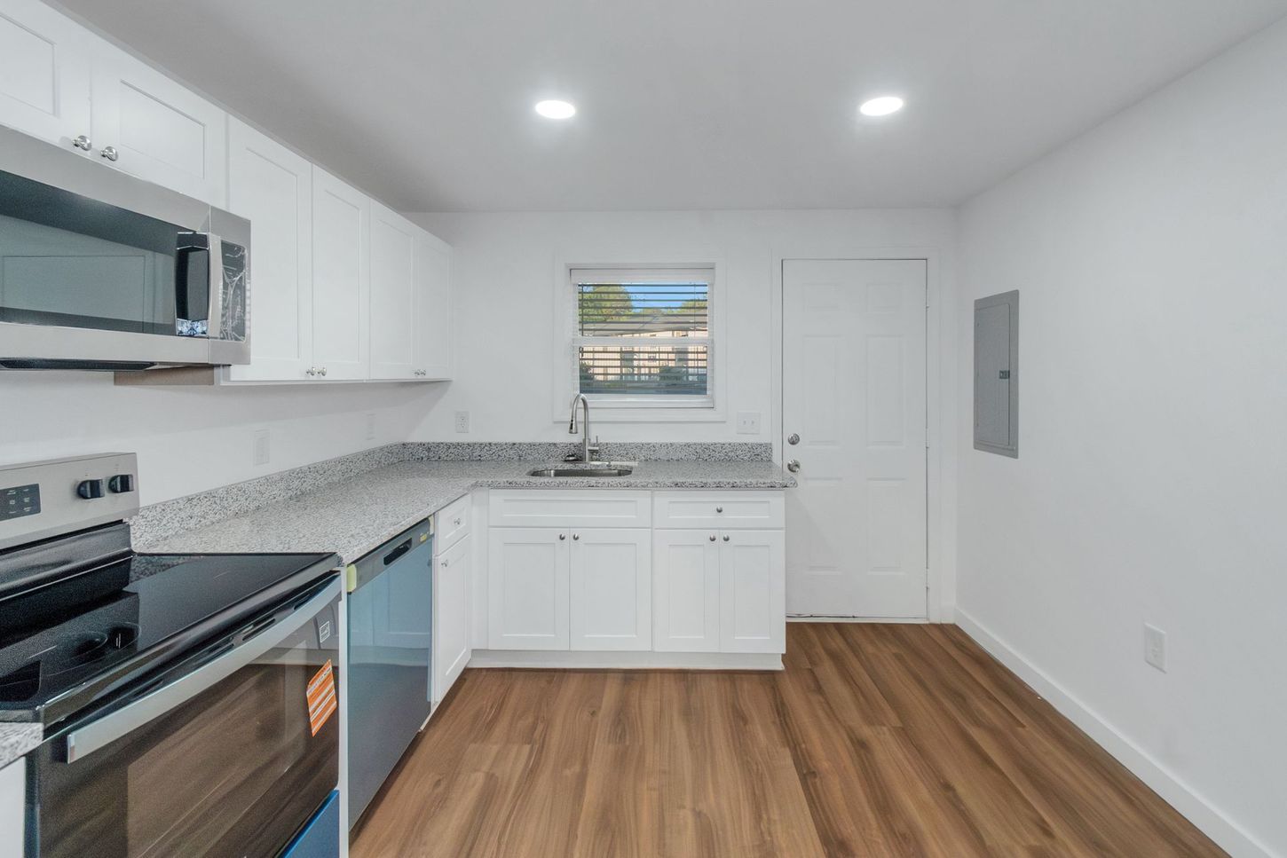 Bright modern kitchen with white cabinets, stainless appliances, granite counters, and wood-look flooring