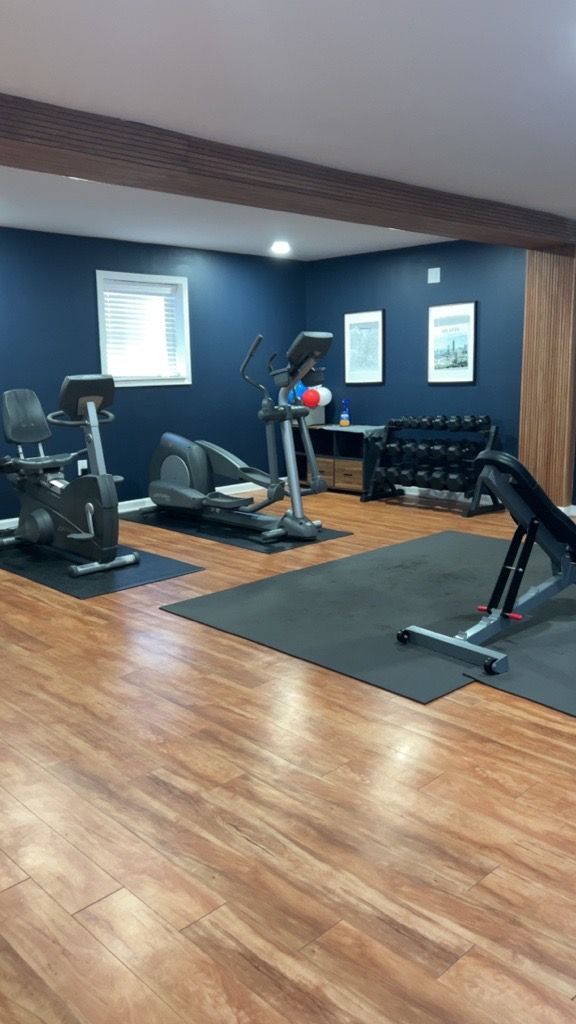Empty gym room with exercise machines, dark blue walls, wood floor, and a black rug area