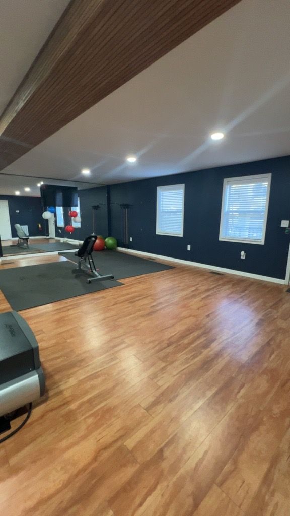 Modern gym room with wood floors, dark walls, windows, and exercise equipment near mirrors