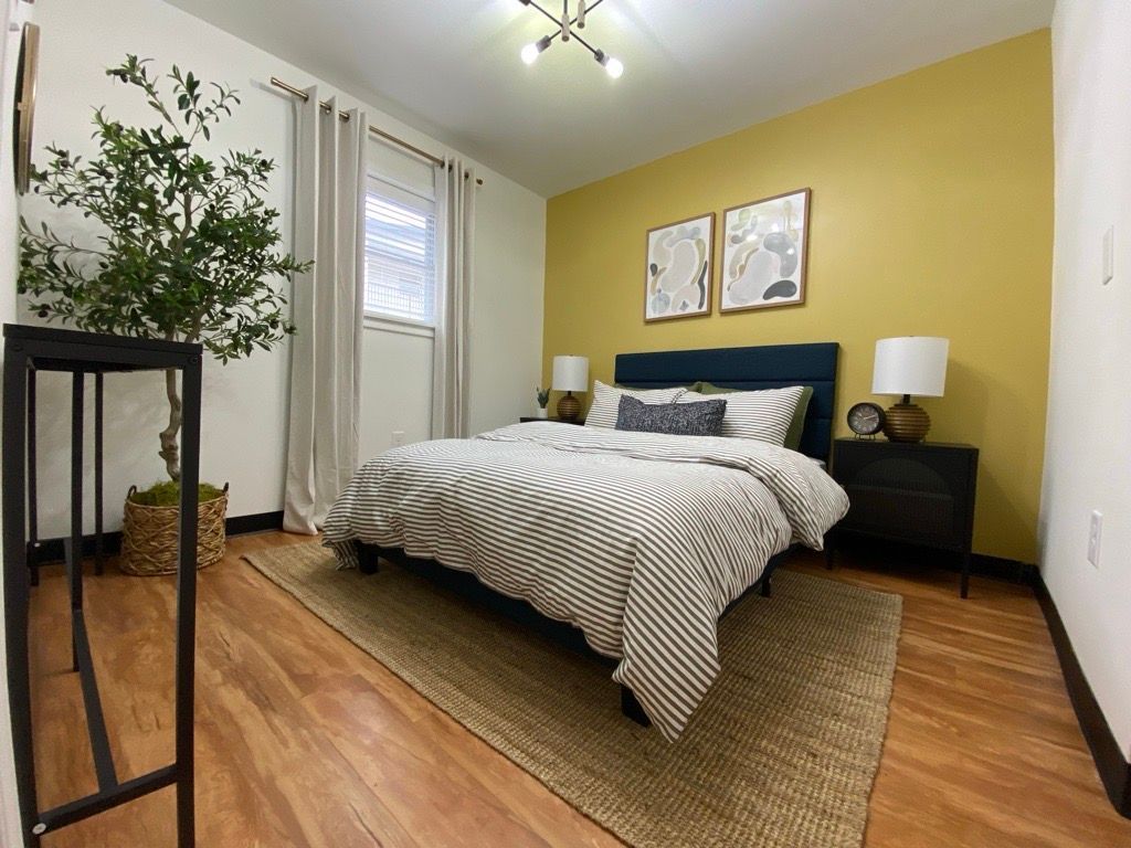 Bright bedroom with a striped bedspread, yellow accent wall, wood floor, and potted plant by the window