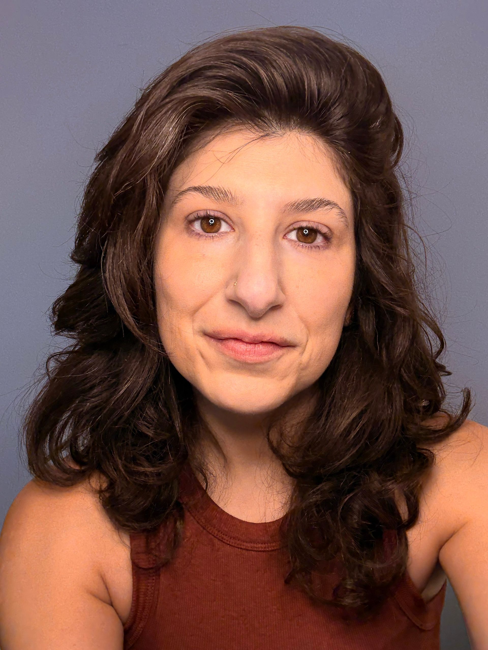 Portrait of a woman with shoulder-length dark hair wearing a rust-colored top against a gray background