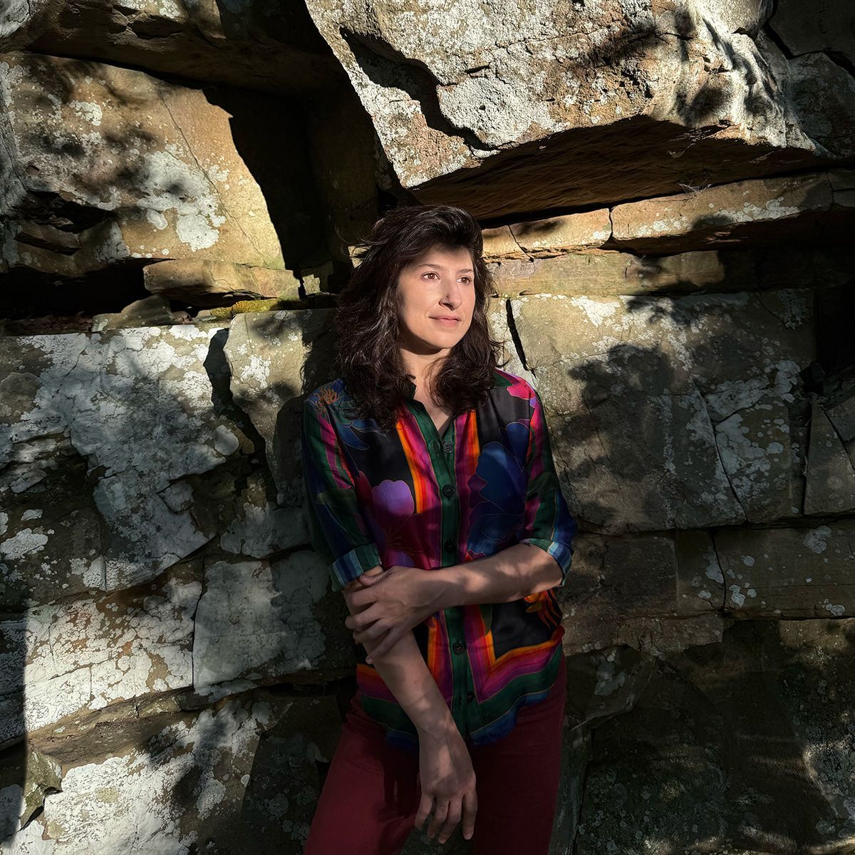 Woman in a colorful top standing against sunlit rock formations outdoors