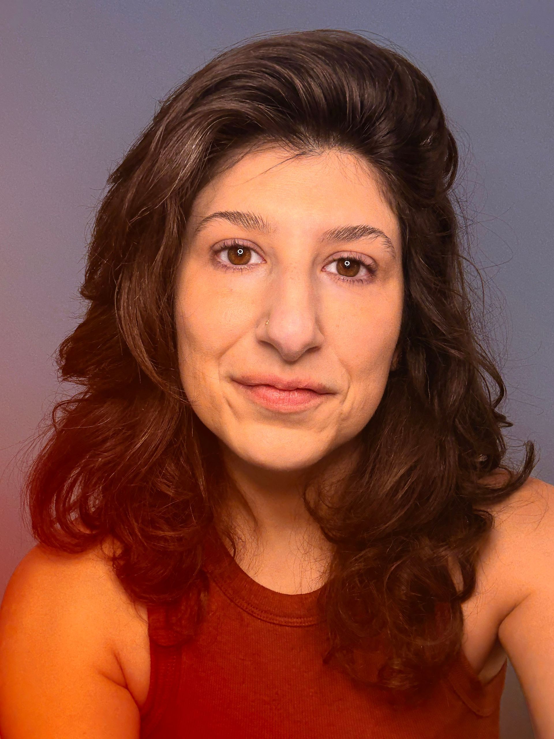 Portrait of a woman with wavy dark hair, wearing a sleeveless red top against a purple background
