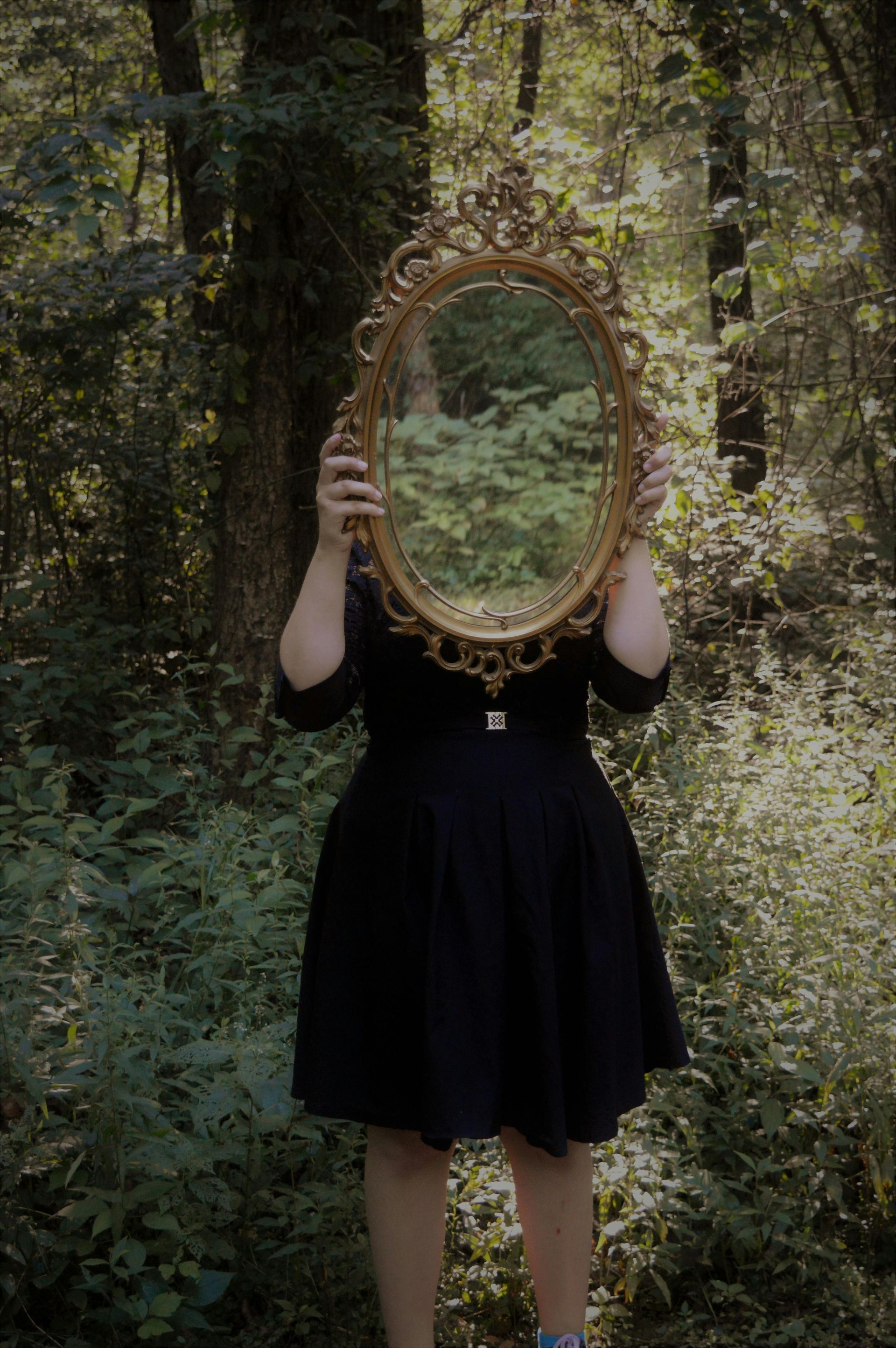spiritual life coach. Woman holding up a mirror. In the forest.