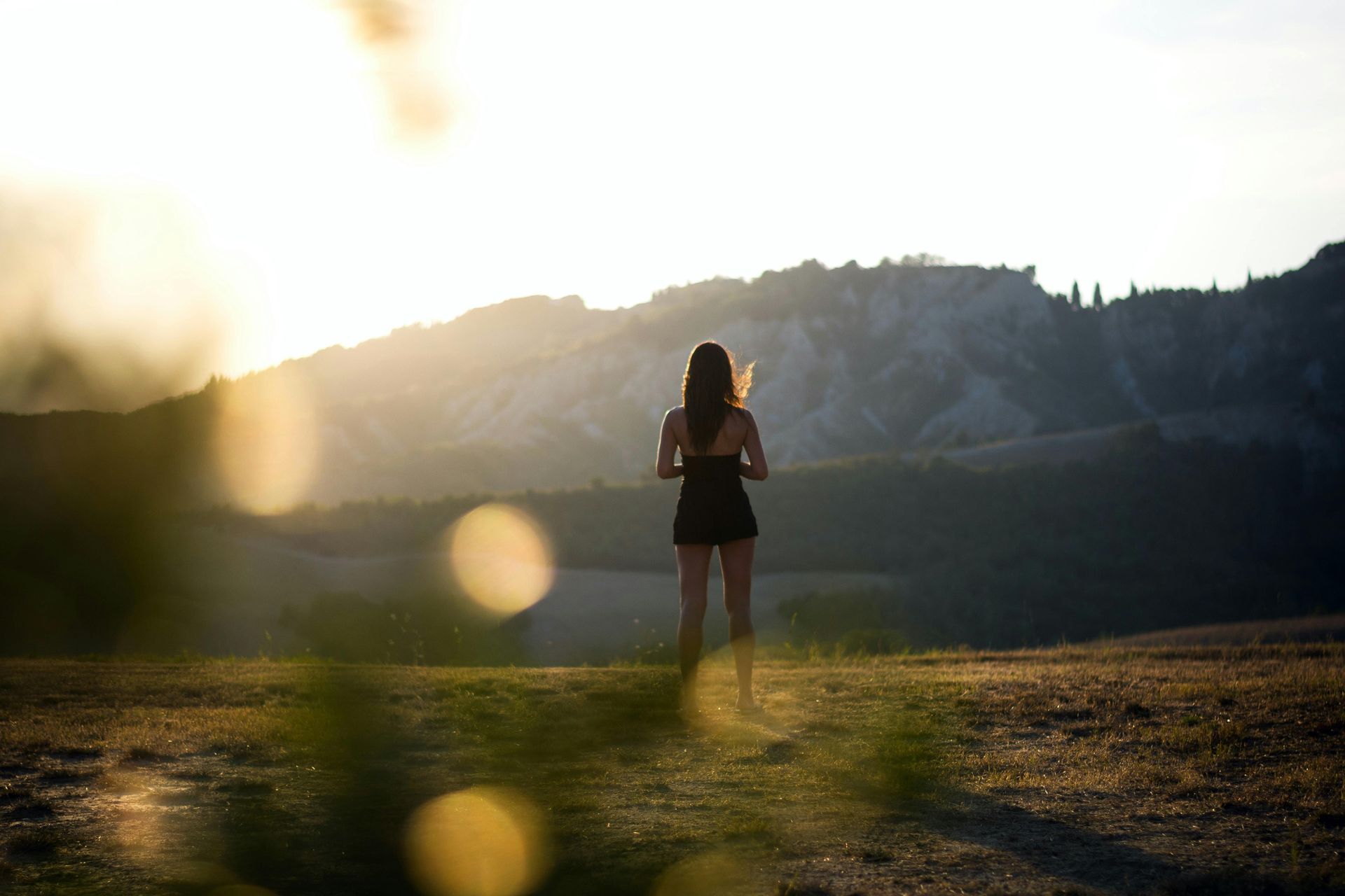 Image of a woman standing in a field in front of mountains. 