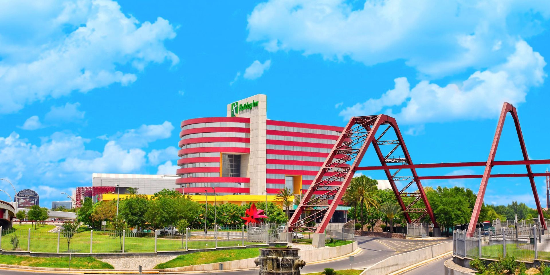 Edificio moderno y colorido con arcos rojos bajo un cielo azul brillante y un paisaje verde.