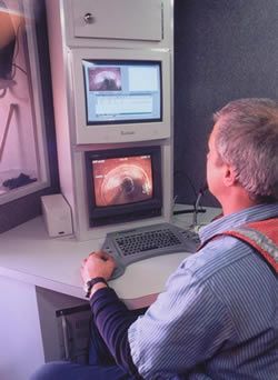 Man operating equipment, viewing monitor with tunnel image, working in a control room.