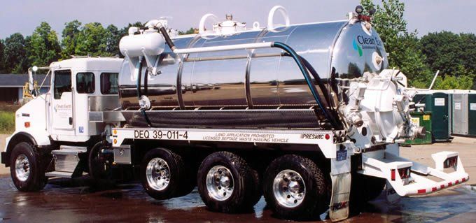 A shiny silver septic service truck parked near portable toilets.