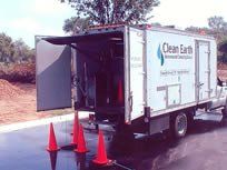 Clean Earth service truck with open rear, cones on wet pavement.