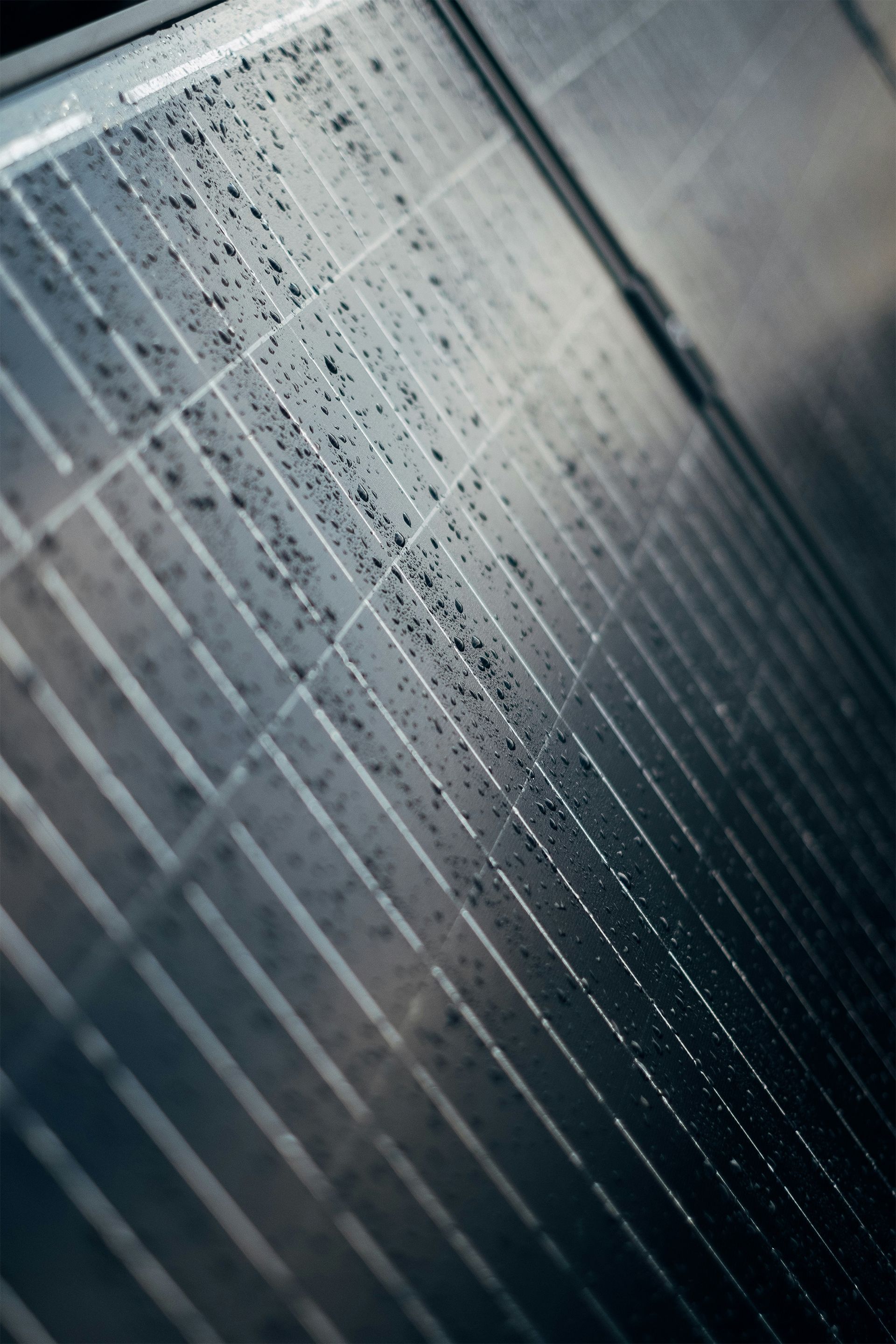 Raindrops on a metal fence or grill, viewed at a diagonal angle in cool gray tones.