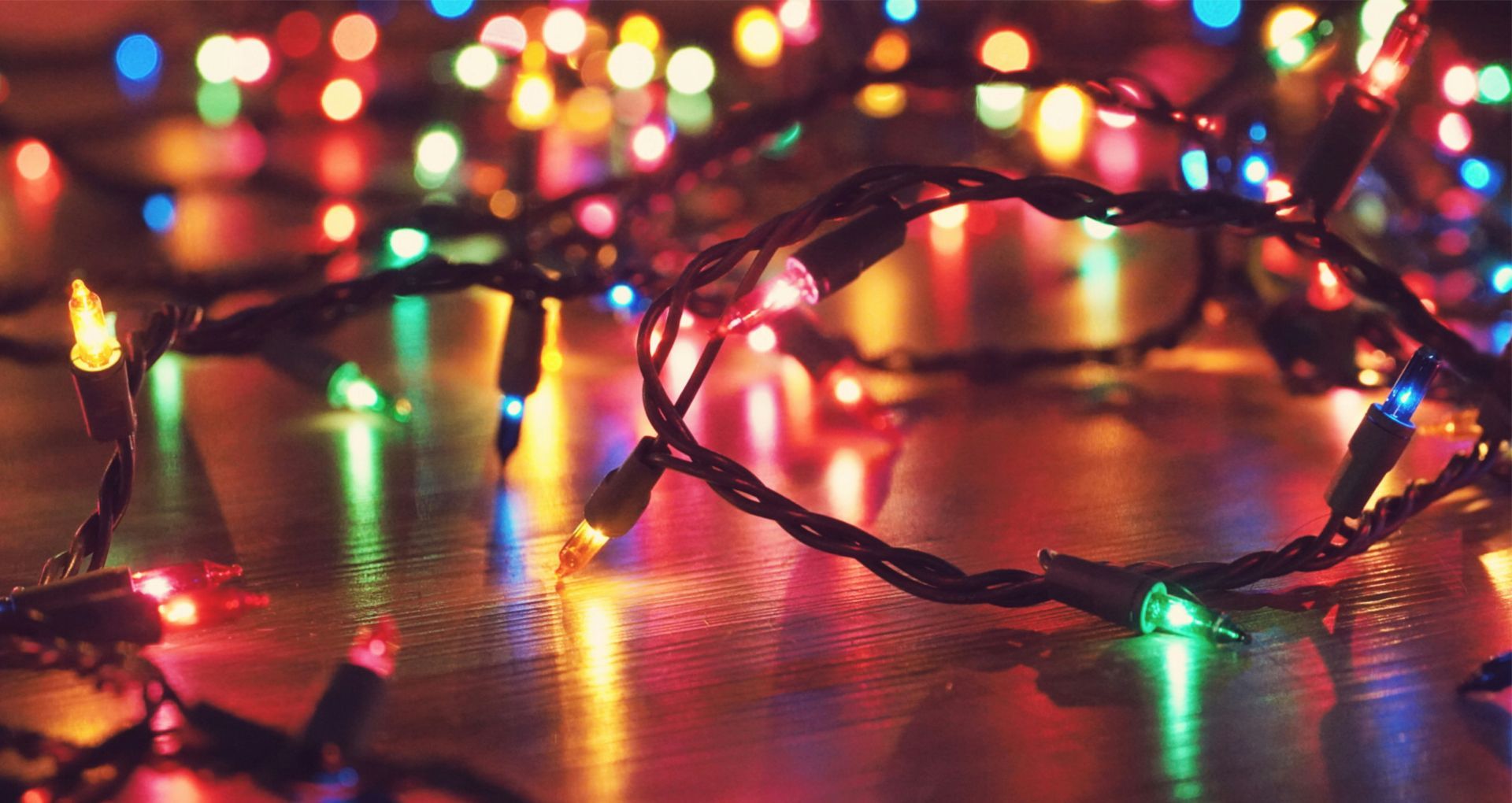 Colorful Christmas string lights coiled on a wooden surface, glowing in red, green, blue, and yellow.