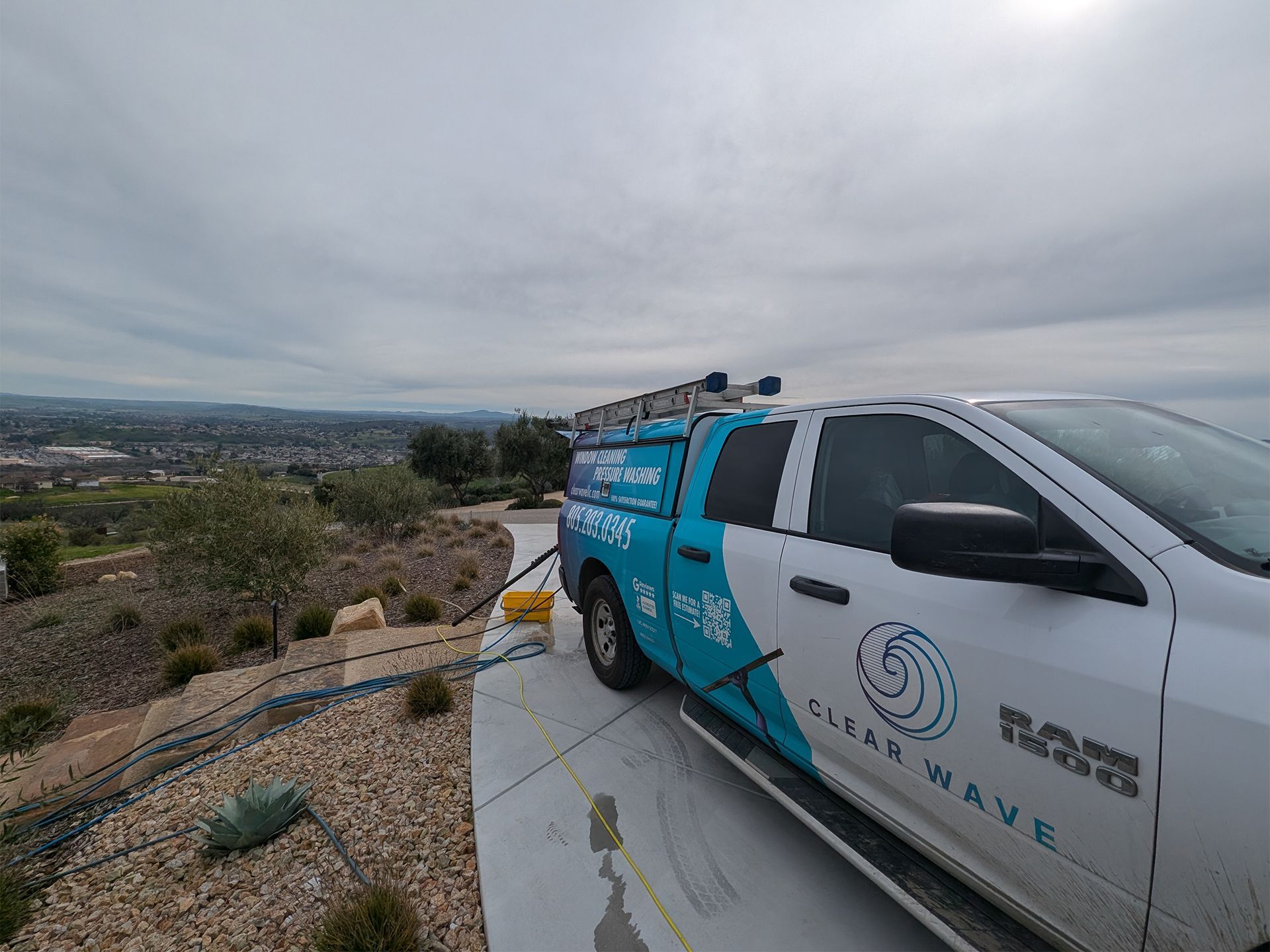 White and blue service truck parked on a rocky overlook above a city under a cloudy sky.