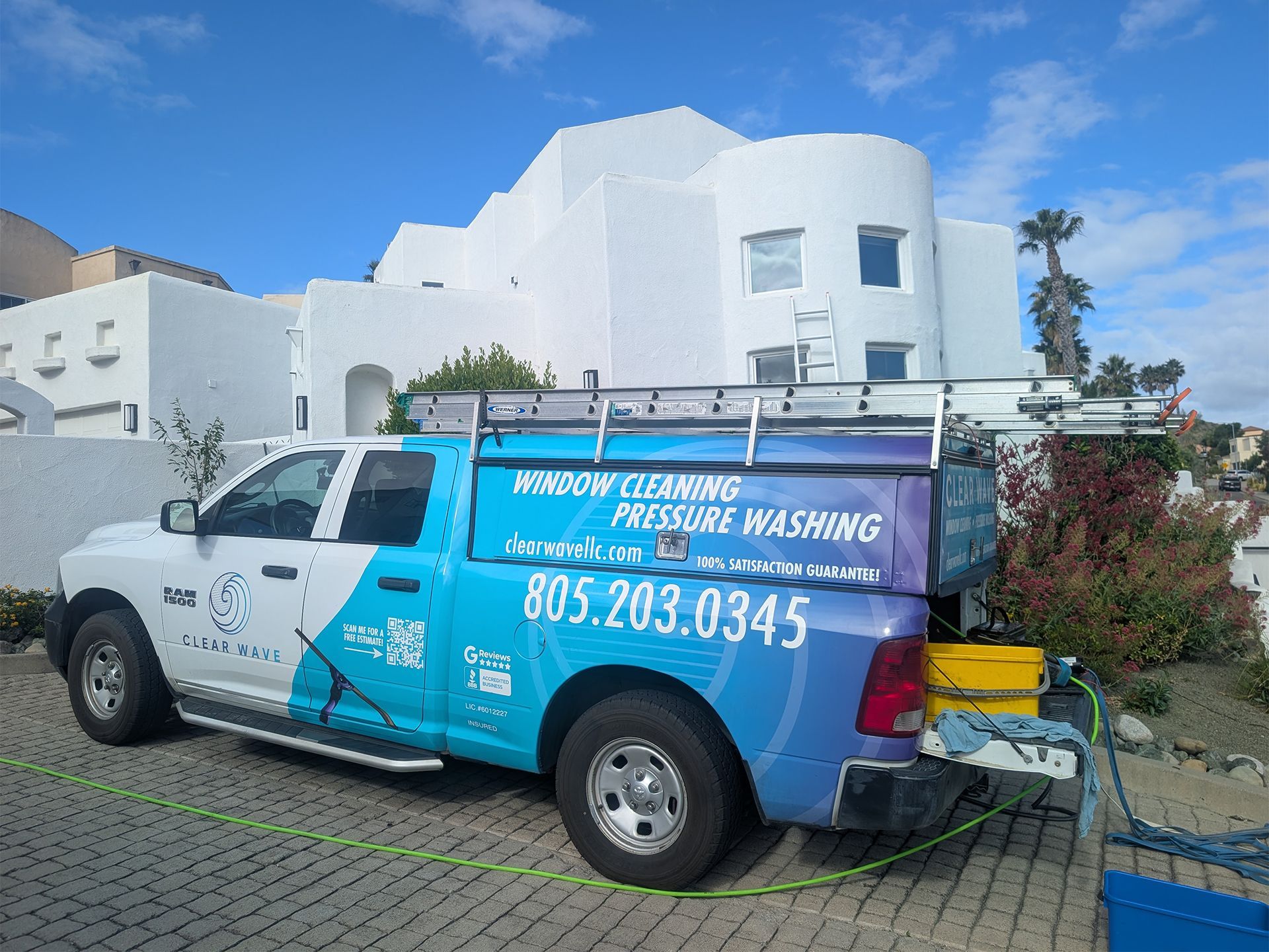 Blue and white cleaning service truck parked by a white stucco house under a clear sky.
