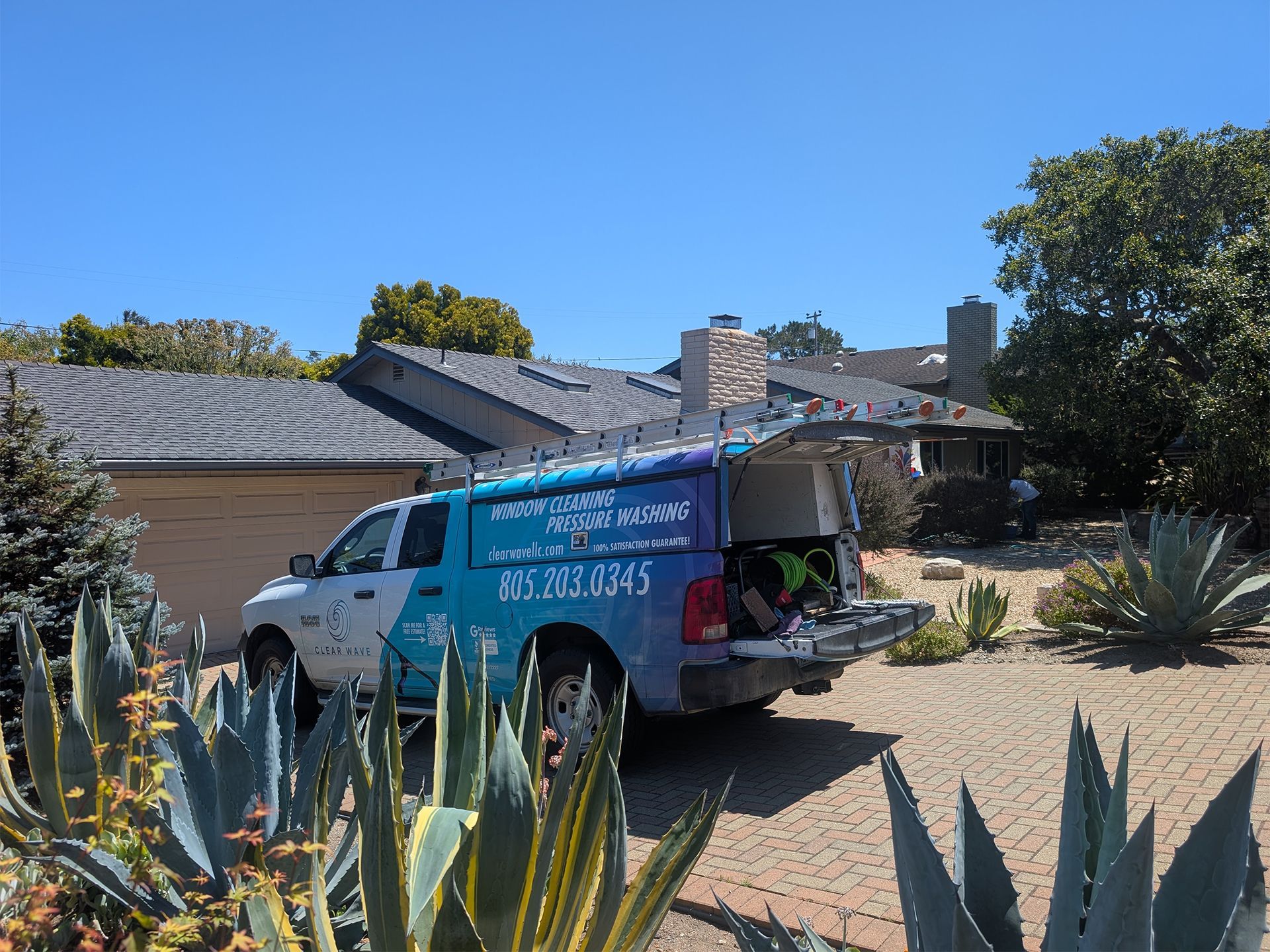 Blue service van parked in a desert front yard beside a house, with agave plants in the foreground.