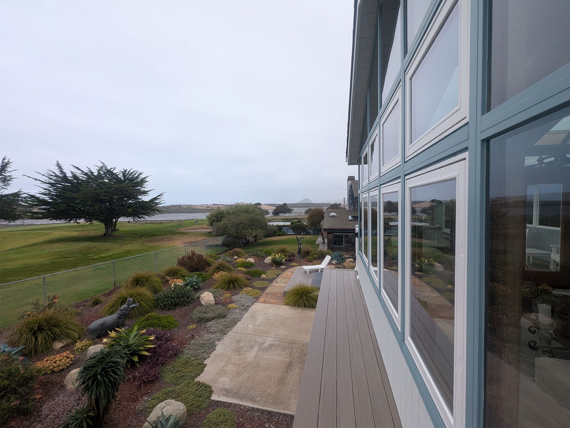 Modern glass building overlooking a landscaped garden and grassy field under an overcast sky.