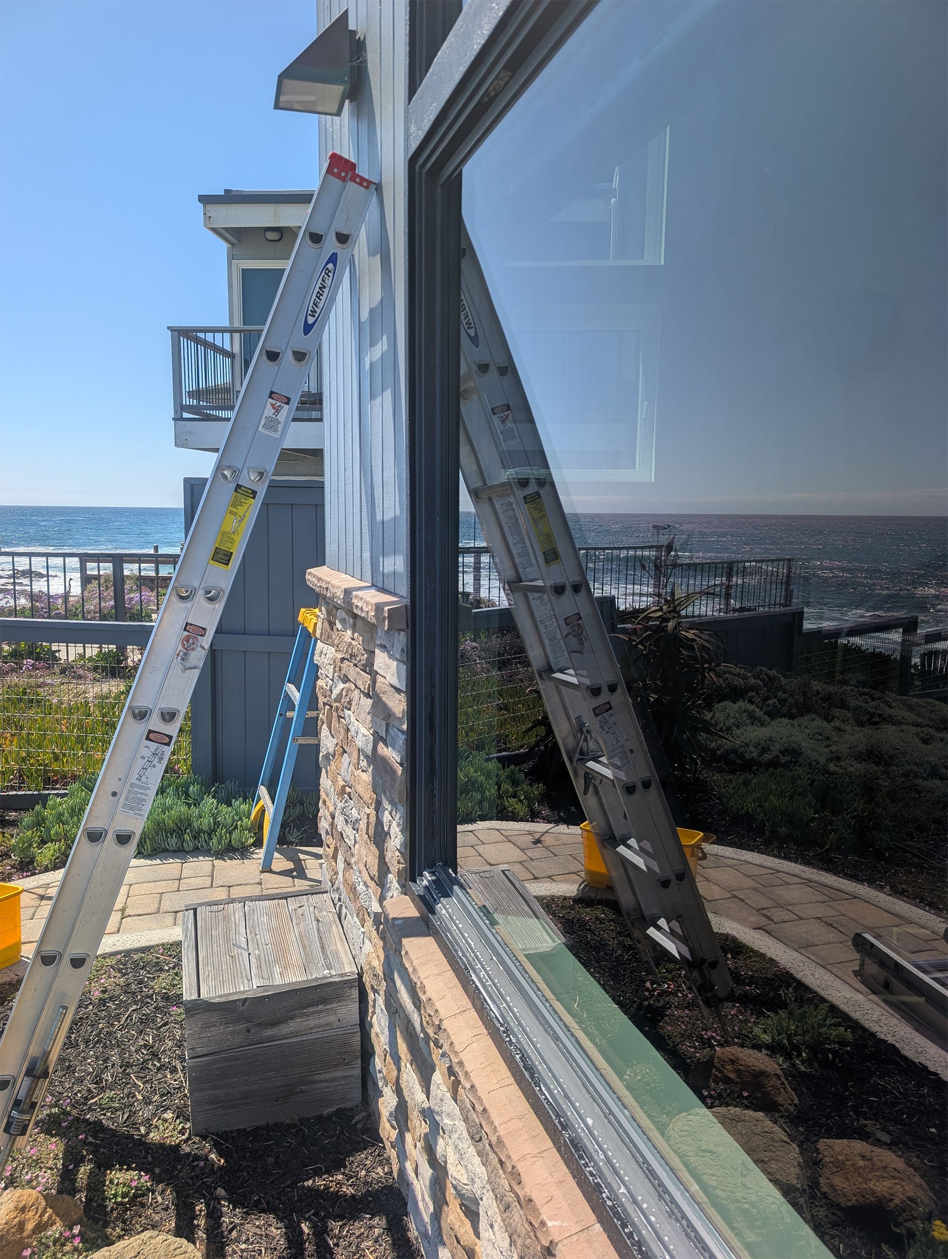 Ladders leaned against a glass building beside a city view, with a blue sky reflected in the windows.