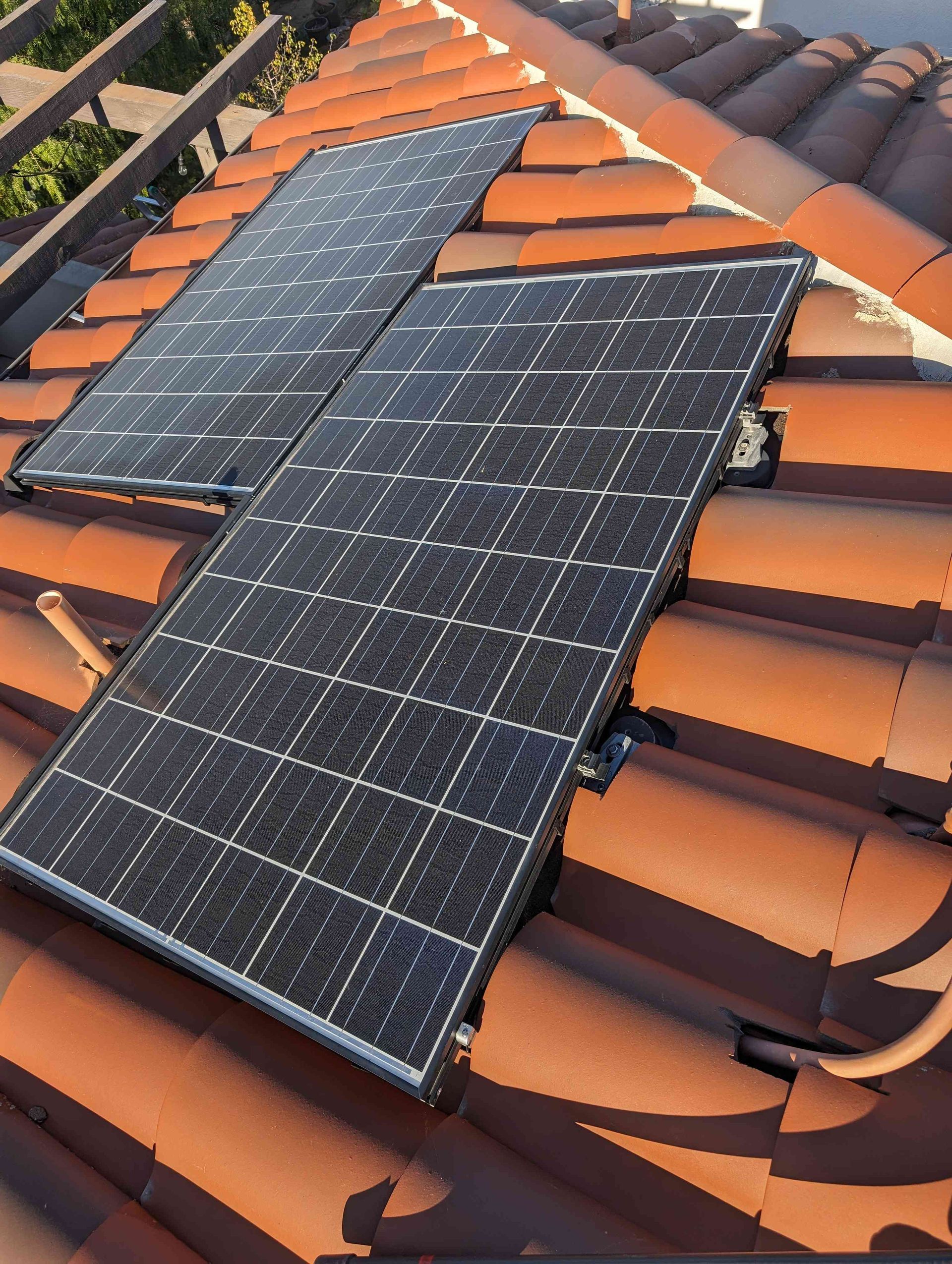 Two solar panels are sitting on top of a tiled roof.