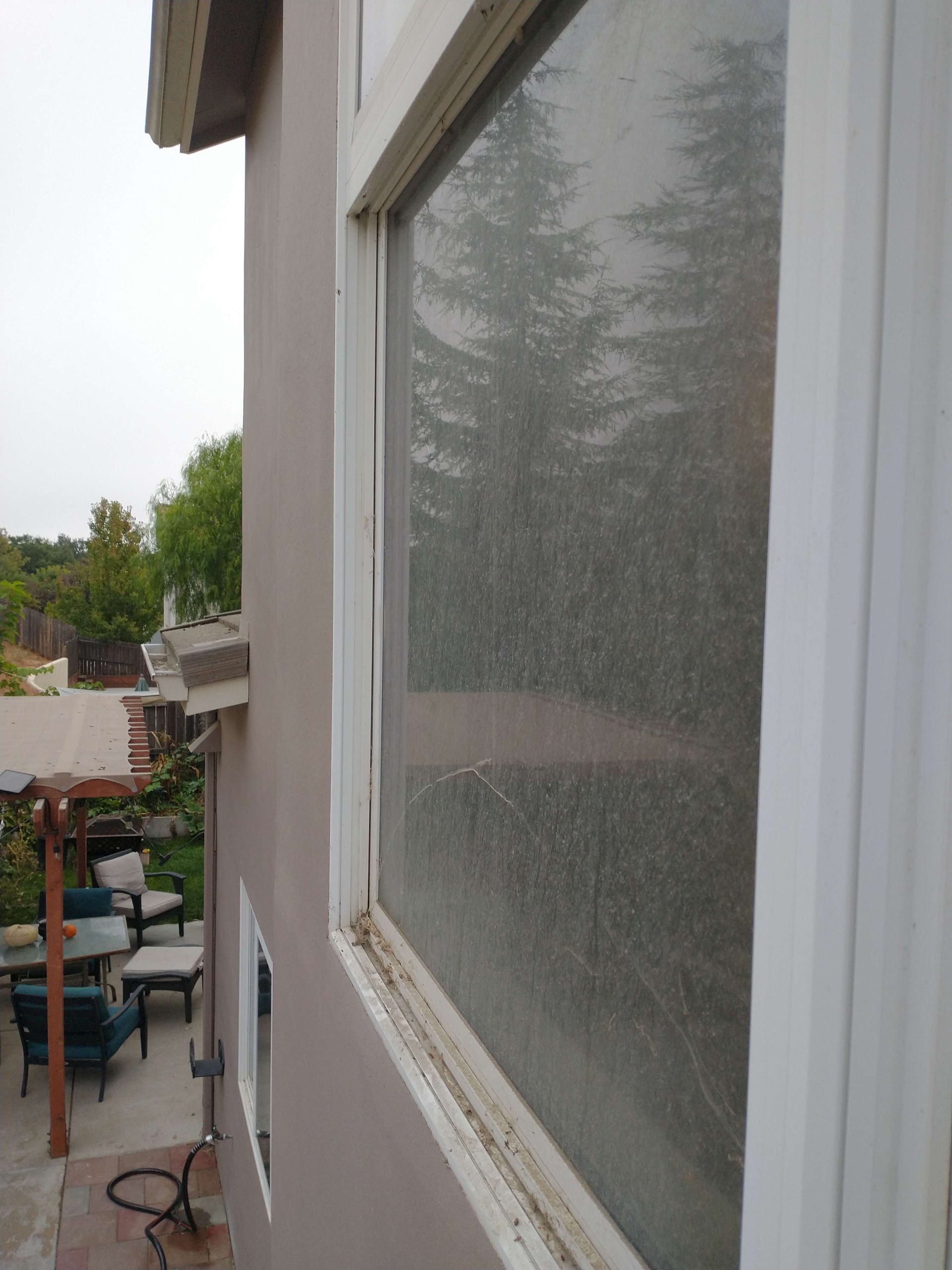 A window on the side of a house with a reflection of trees in it.