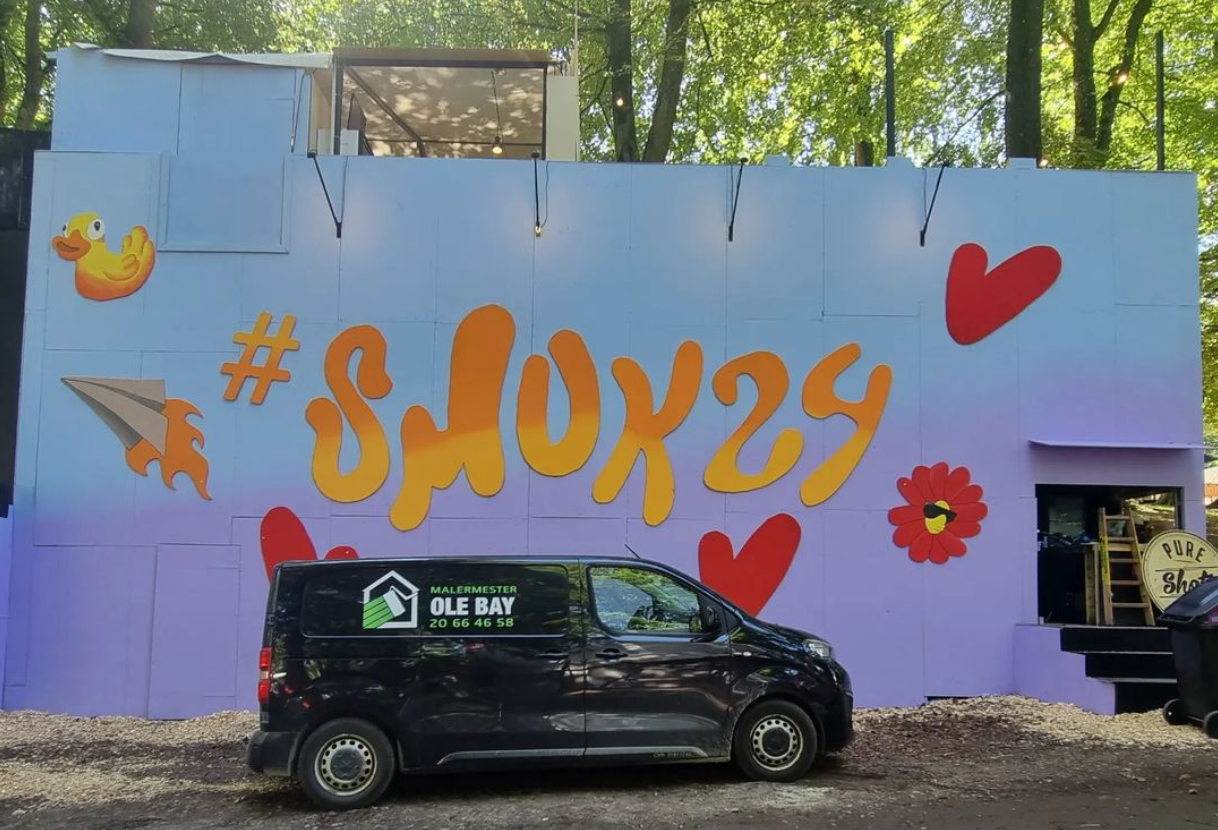 En sort varevogn er parkeret foran en lilla væg, hvor der står snox29