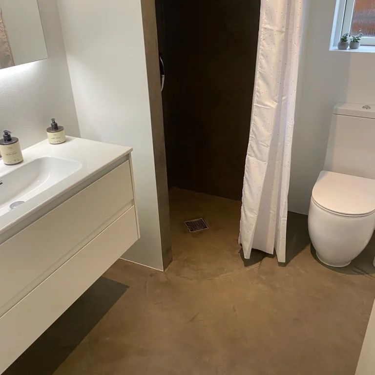 Et badeværelse med toilet, håndvask og bruseforhæng.
