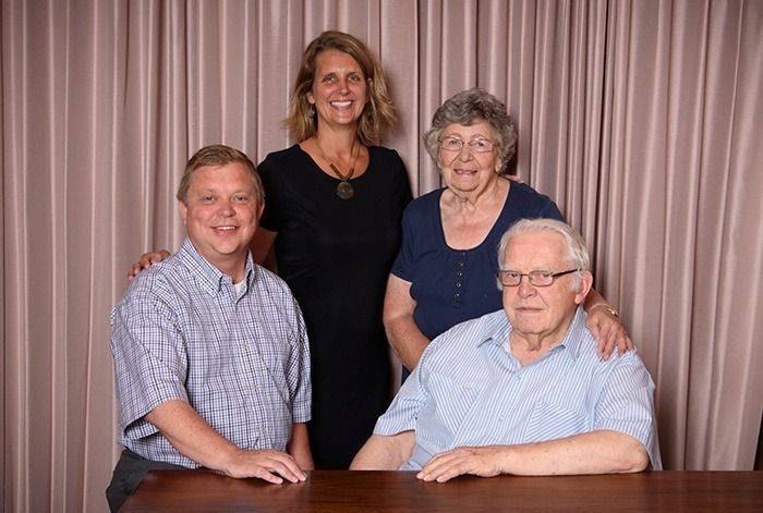 Family portrait: four people smiling, posed behind a table in front of a curtain.