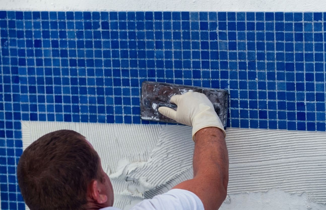 Worker troweling white mortar over blue pool tiles