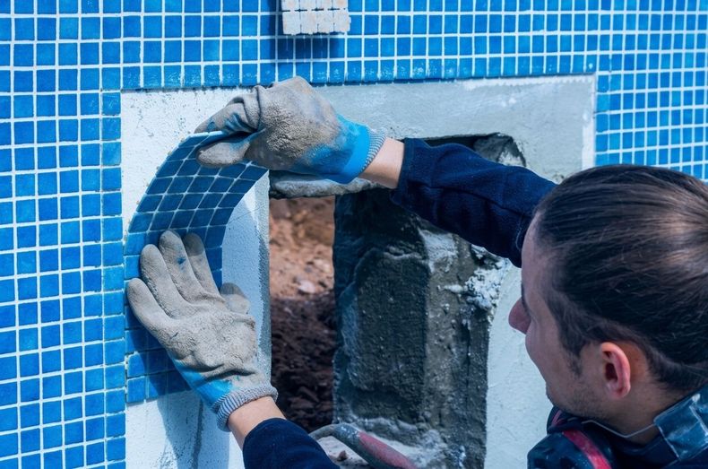 Worker installing blue mosaic tile around a window opening