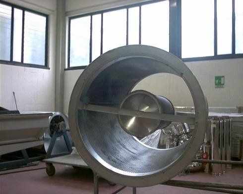 Grande ventilatore industriale in metallo all'interno di un locale di fabbrica con finestre e tubi