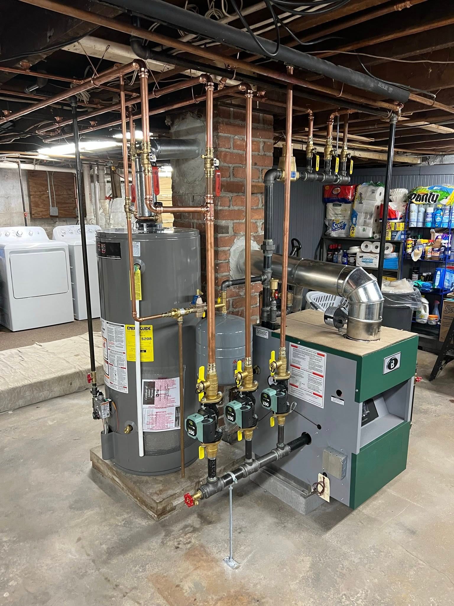 A grey water heater and a green gas boiler connected by copper piping in a basement utility area.