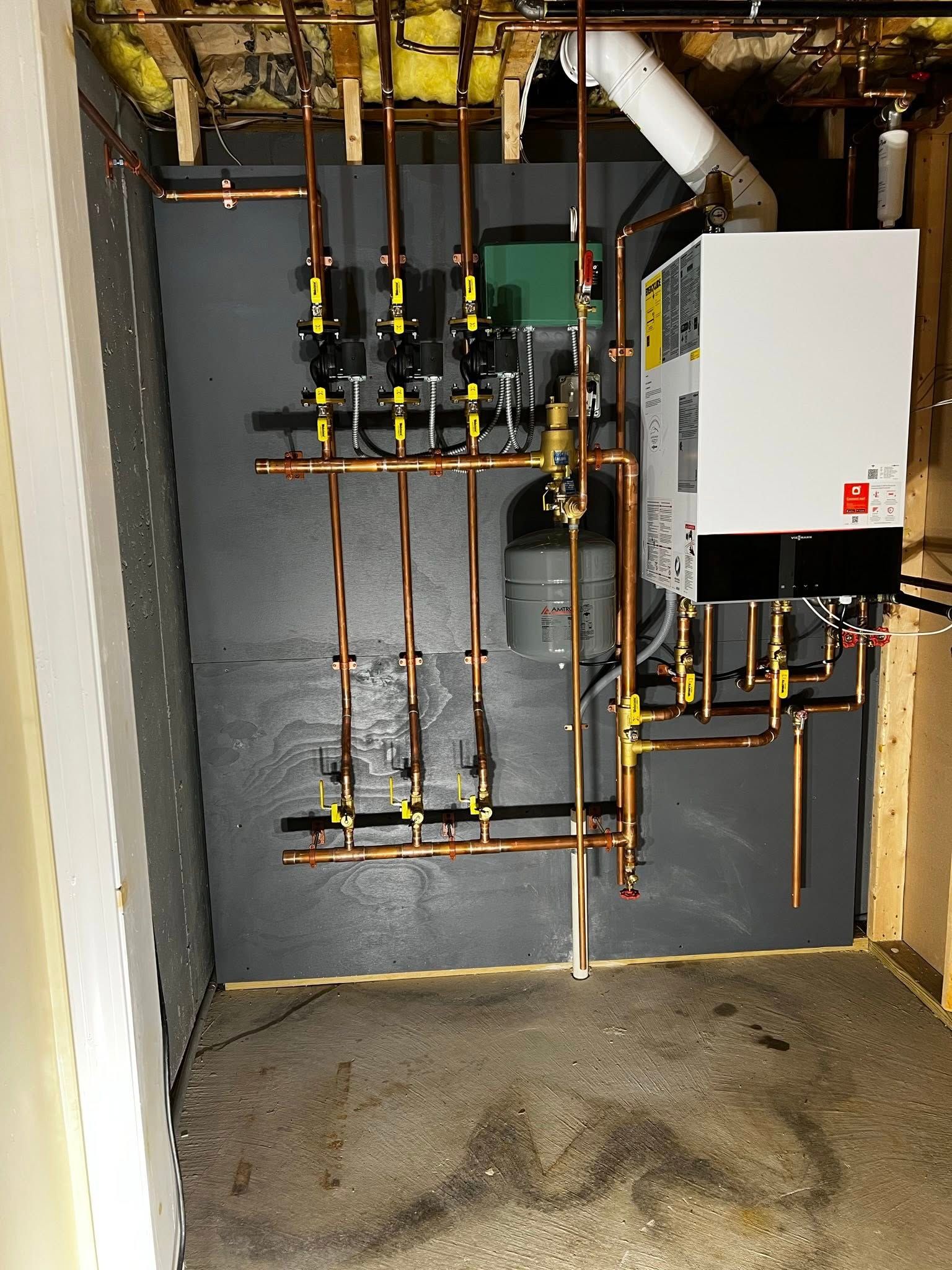 A wall-mounted boiler and copper piping system with multiple pump valves and a small expansion tank in a utility room.