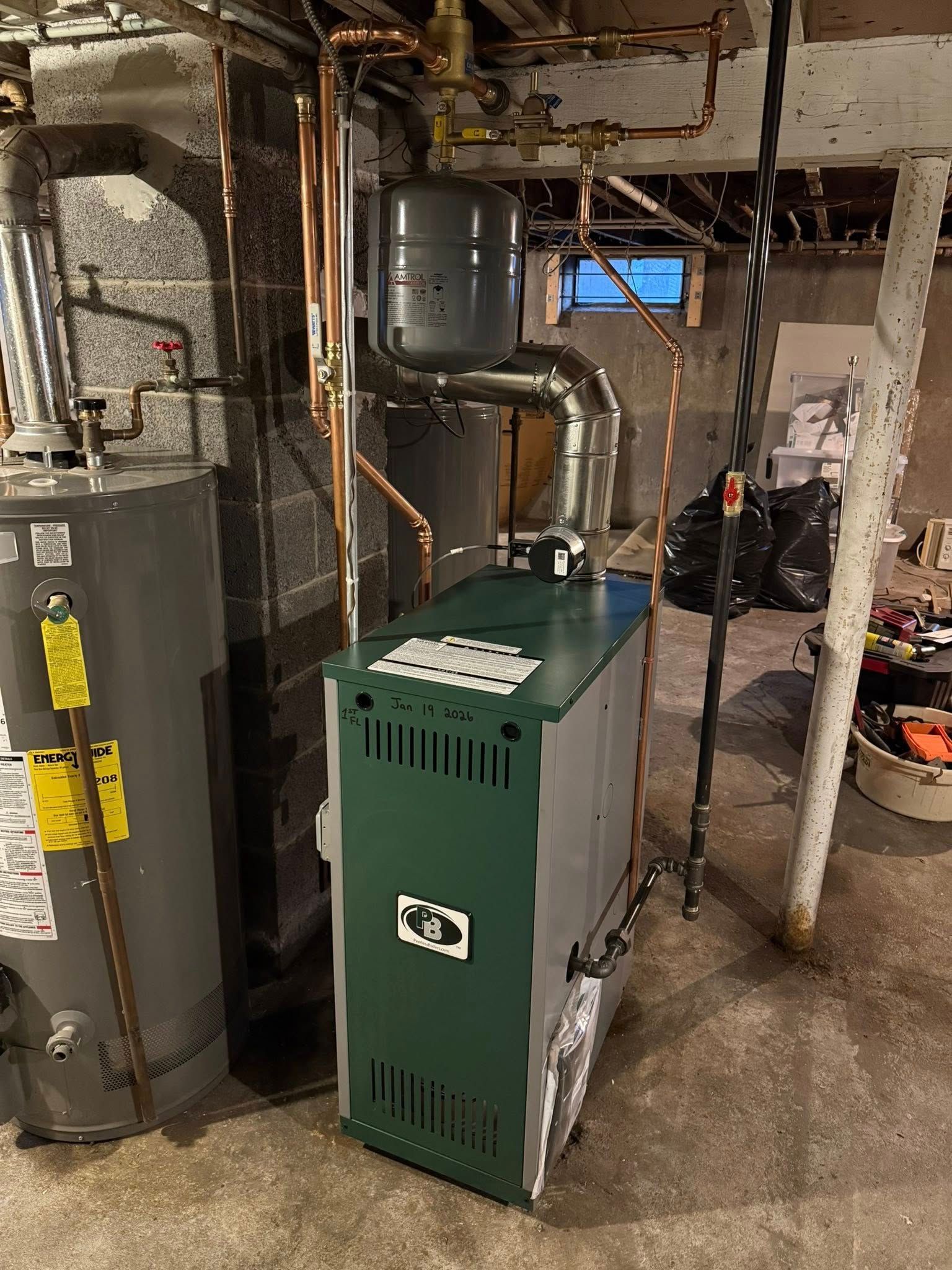 A grey and green residential boiler and water heater in a basement with visible copper piping and ductwork.