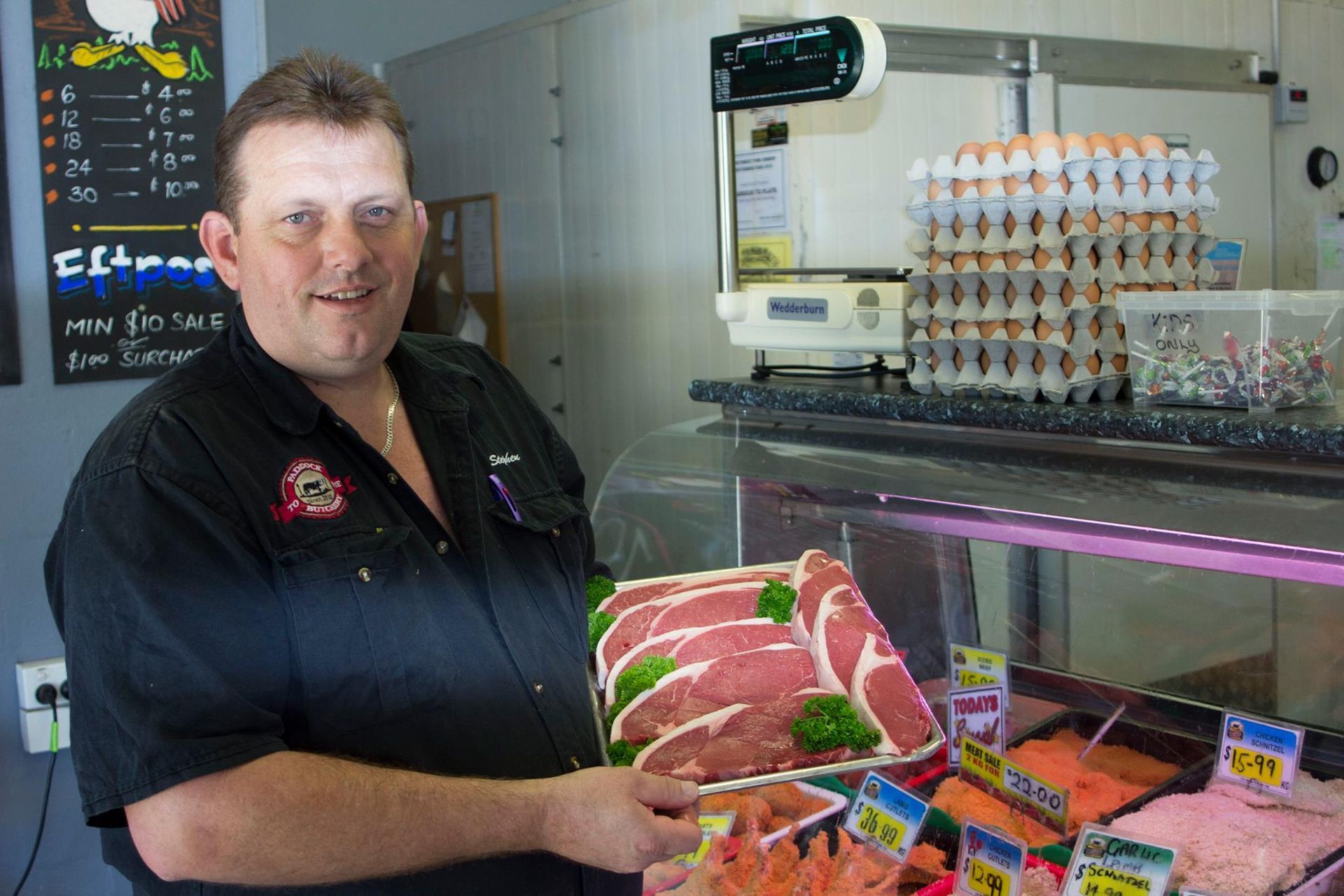 A Butcher Standing Behind a Meat Display Counter, Holding a Tray of Steaks — Paddock to Plate in Tamworth, NSW