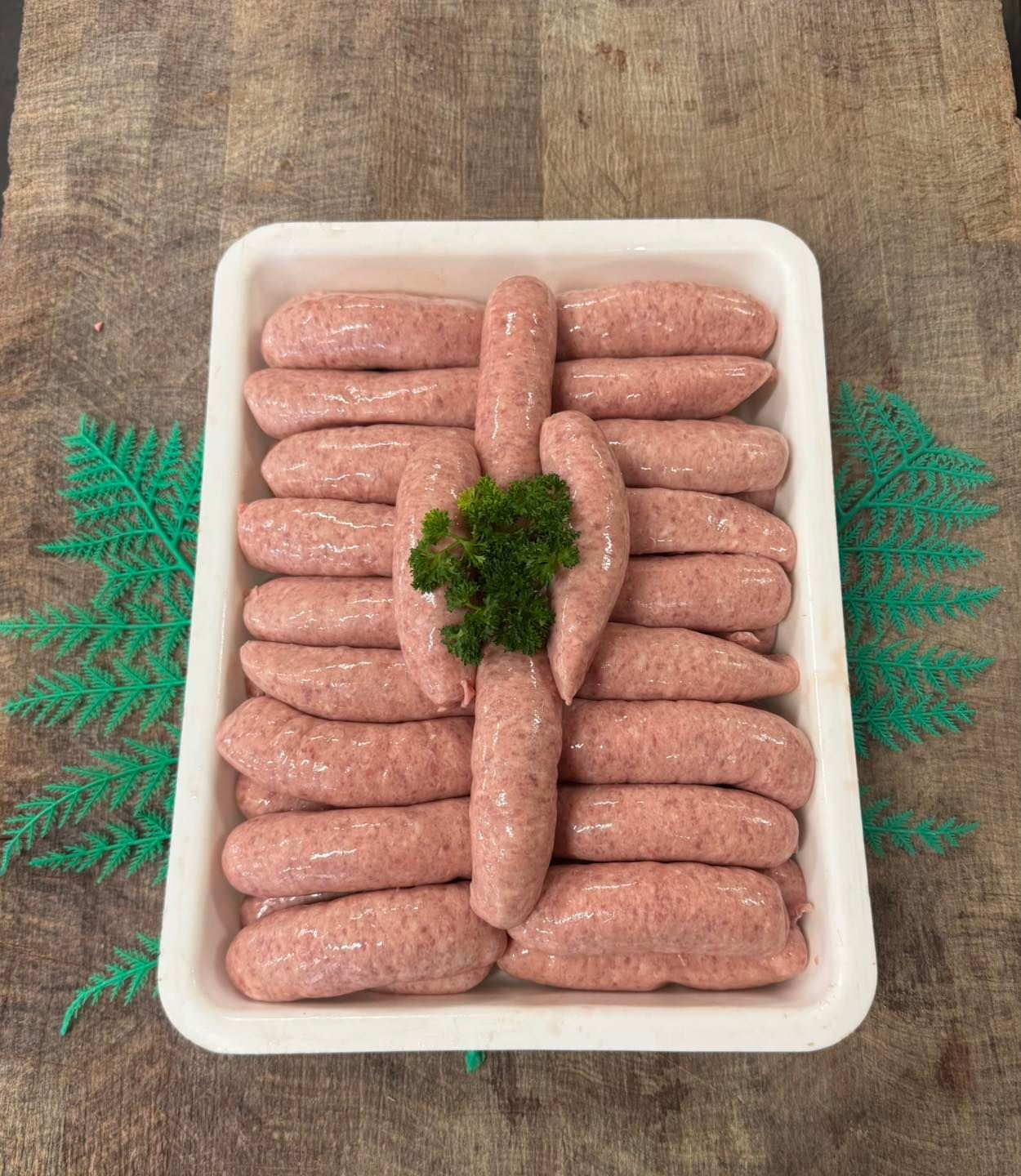 A Tray of Raw Sausages With a Sprig of Parsley on a Wooden Surface — Paddock to Plate in Tamworth, NSW