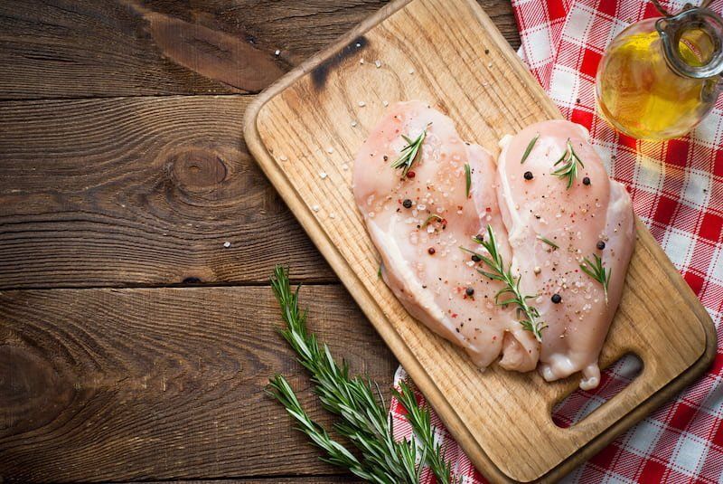 A Raw Chicken Breasts Seasoned With Rosemary, Salt, and Pepper on a Wooden Cutting Board — Paddock to Plate in Tamworth, NSW