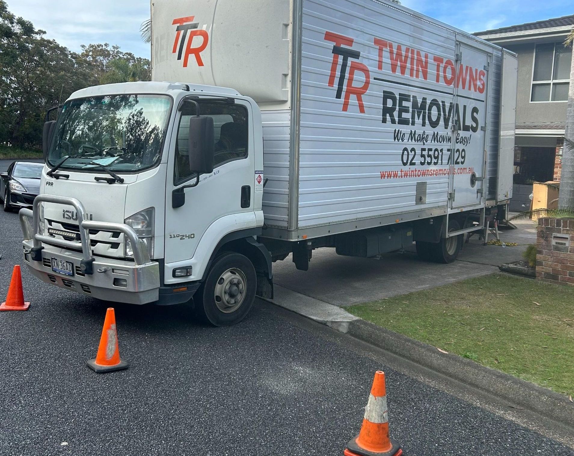 Two Men Are Lifting A Chair That Is Covered In Plastic Wrap — Twin Towns Removals Mid North Coast In Tuncurry, NSW