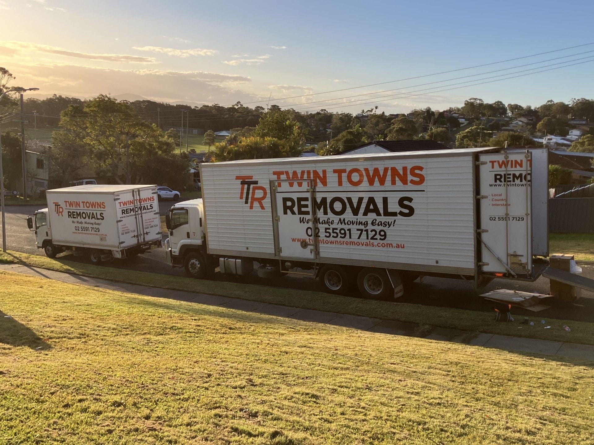 Two White Removals Trucks Parked Next to Grass At Sunset - Twin Towns Removals Mid North Coast In Forster, NSW