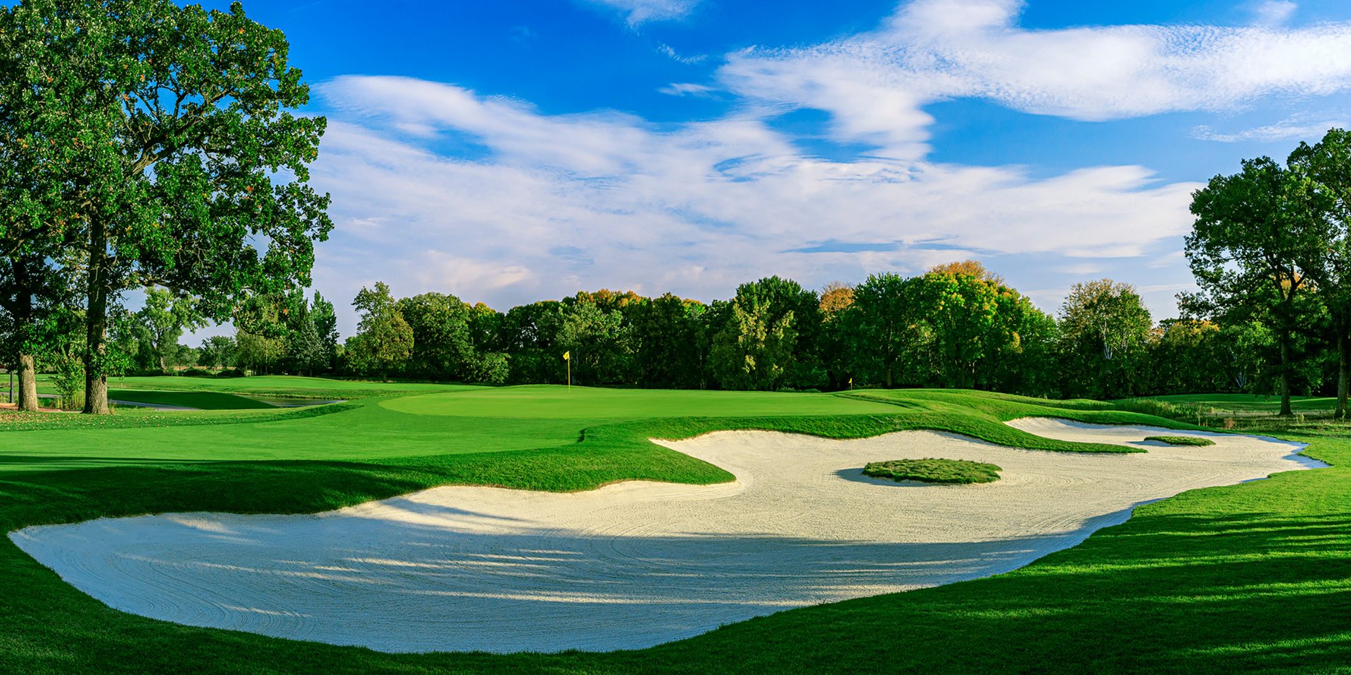A golf course with a bunker in the middle of it and trees in the background.