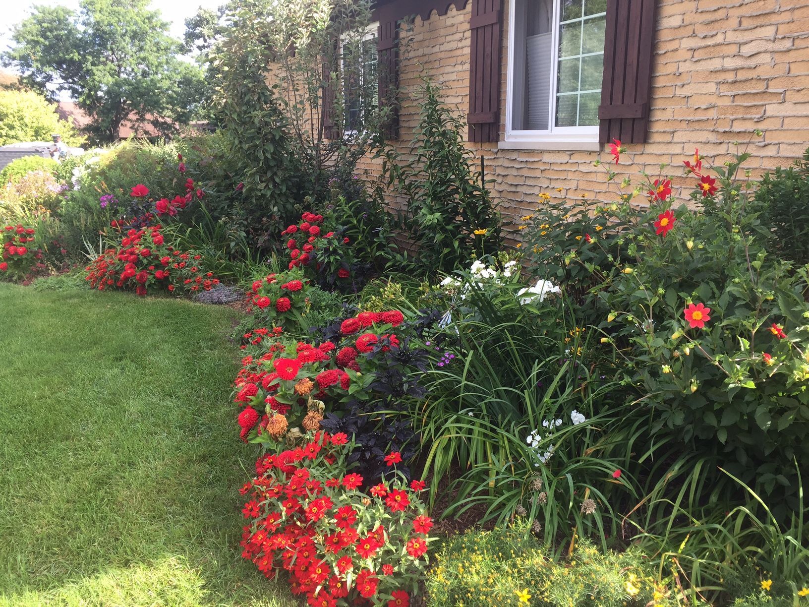 A brick house with a lush green lawn and flowers in front of it.