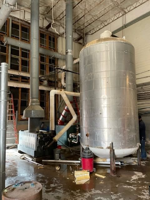 Industrial facility with a large silver tank, black machine, and wet floor in a factory interior