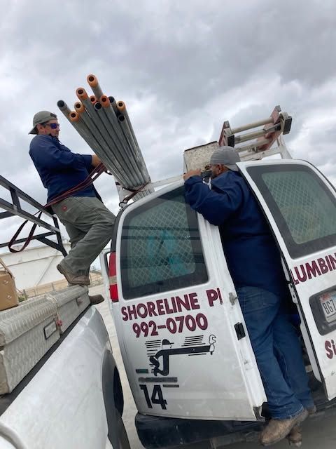 Two workers loading metal pipes onto a white service truck at a cloudy work site.