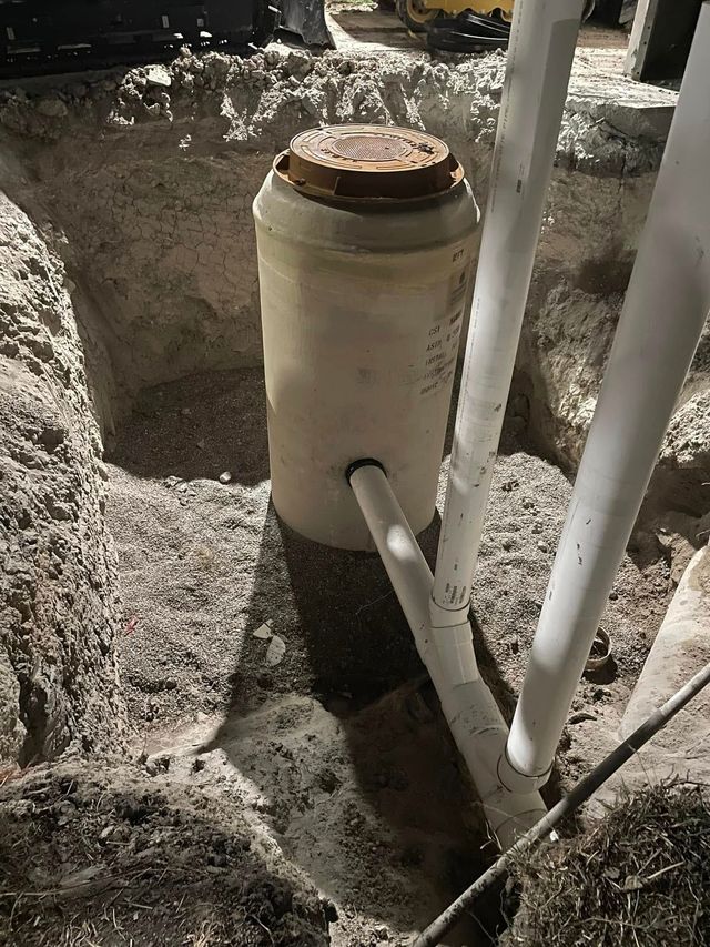 Tall white utility cylinder with pipes, standing in gravel at night near a landscaped area