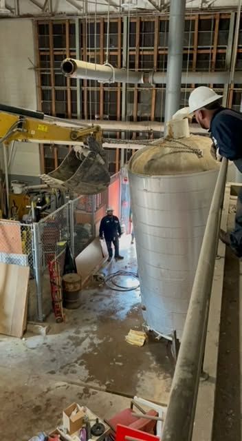 Industrial site with large metal tank, scaffolding, and workers in a narrow construction area