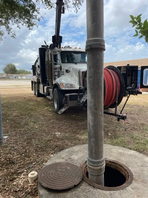 White utility truck with a red hose reel parked near a utility pole and open manhole on a grassy roadside