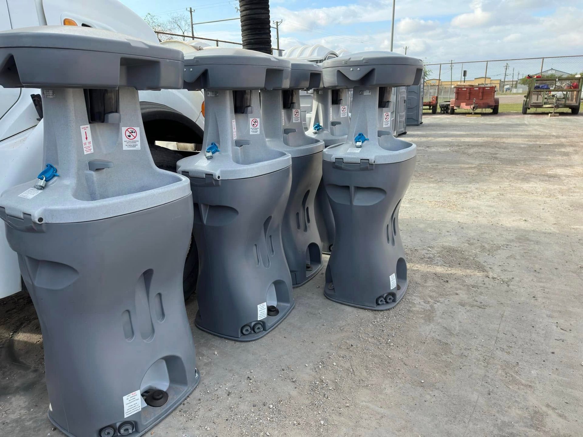 Gray industrial machines or equipment lined up outdoors on a gravel lot under a bright sky