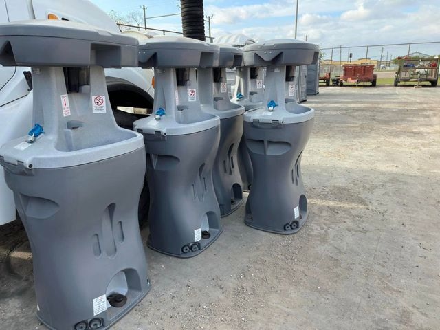 Gray industrial machines or equipment lined up outdoors on a gravel lot under a bright sky